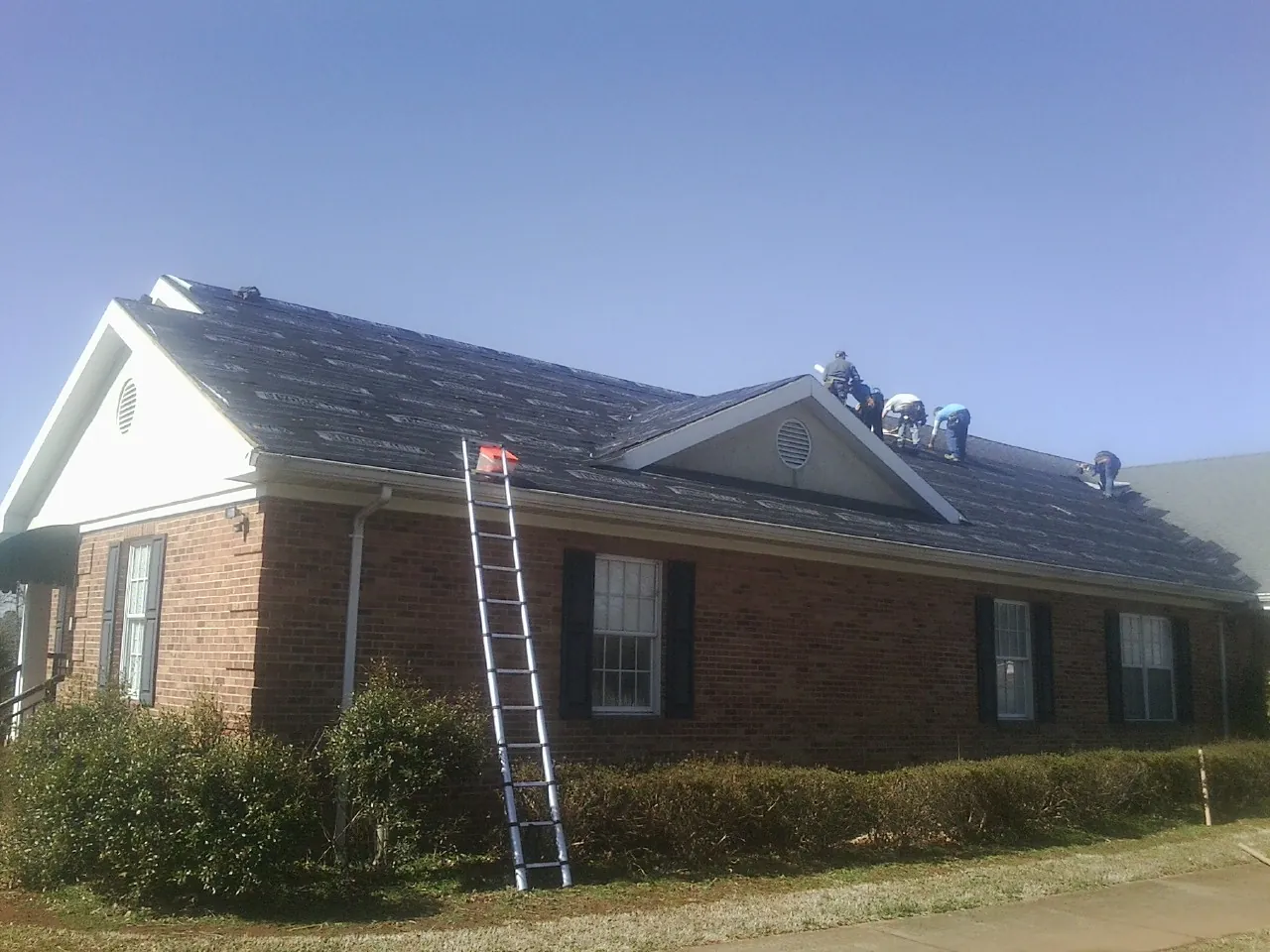Crew tearing shingles off a brick ranch roof with a ladder set — Metal Roof Repair work by our crew in Gladwyne