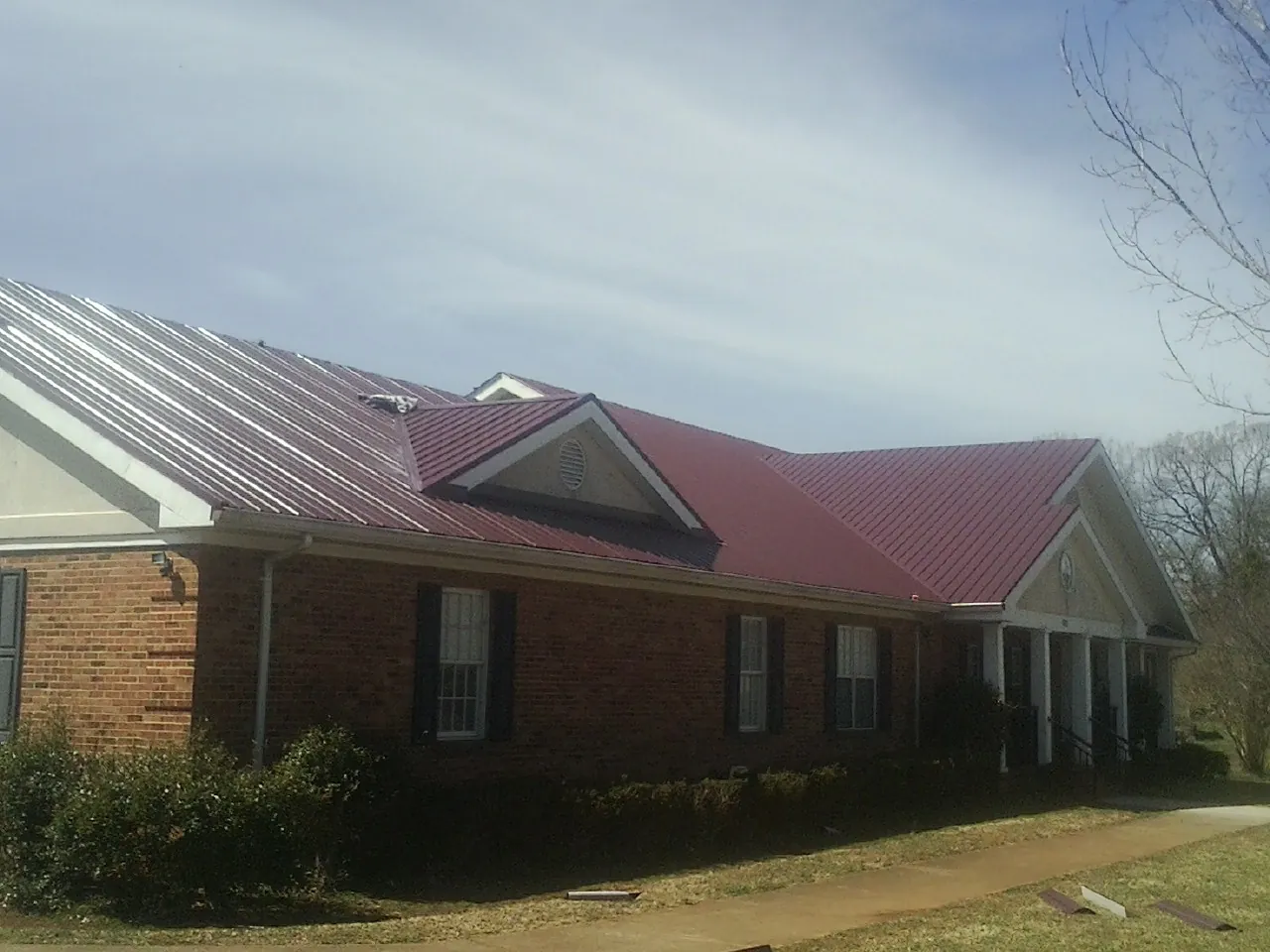 Red metal roof with gabled entries on a long brick building, from a Hail Damage Roof Repair job in Gladwyne