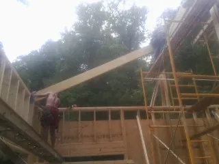 Carpenter raising a rafter beam on a new second story frame in Gladwyne