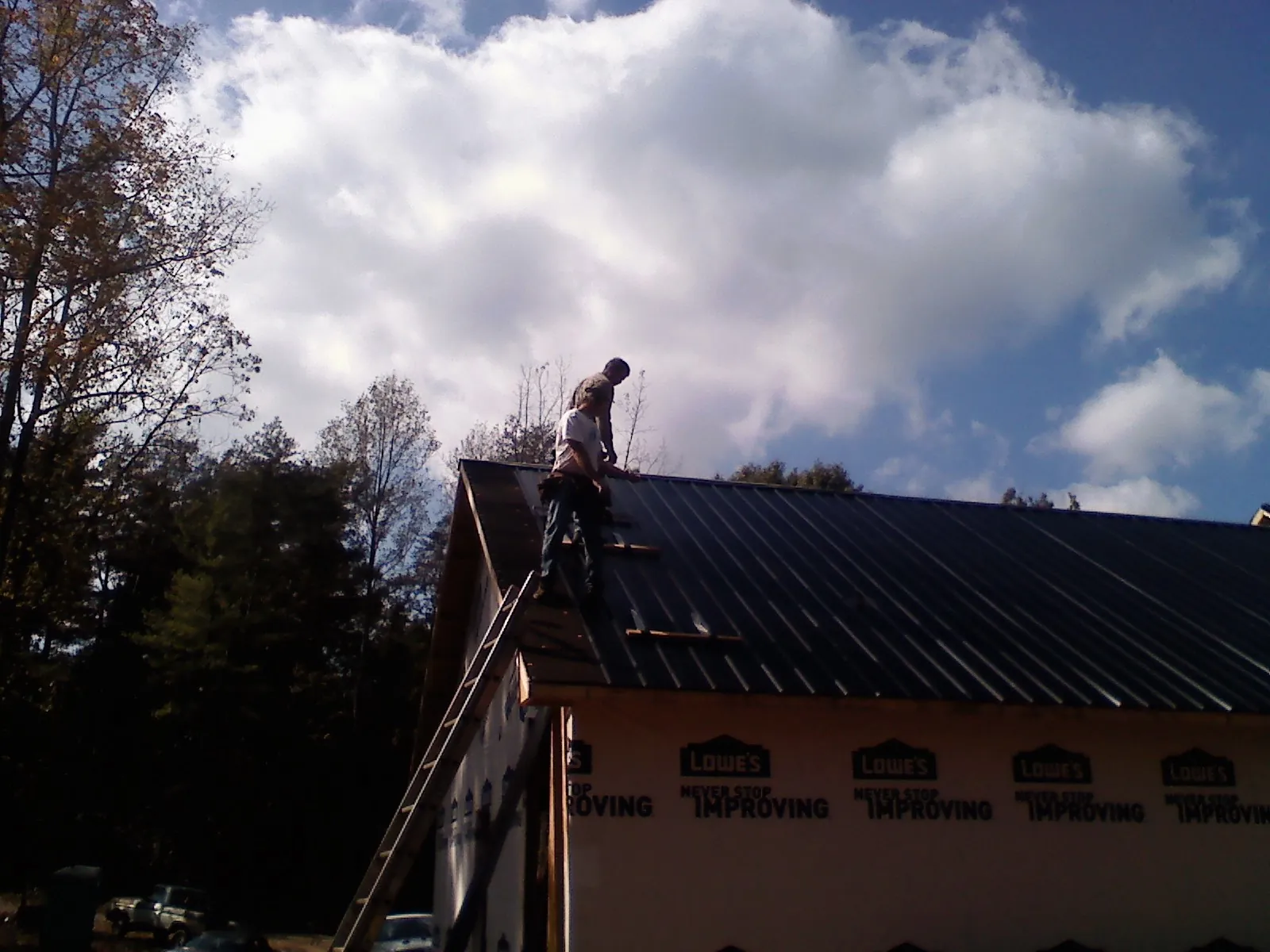 Roofer fastening dark metal panels high against a cloudy sky, from a Roof Inspection job in Gladwyne