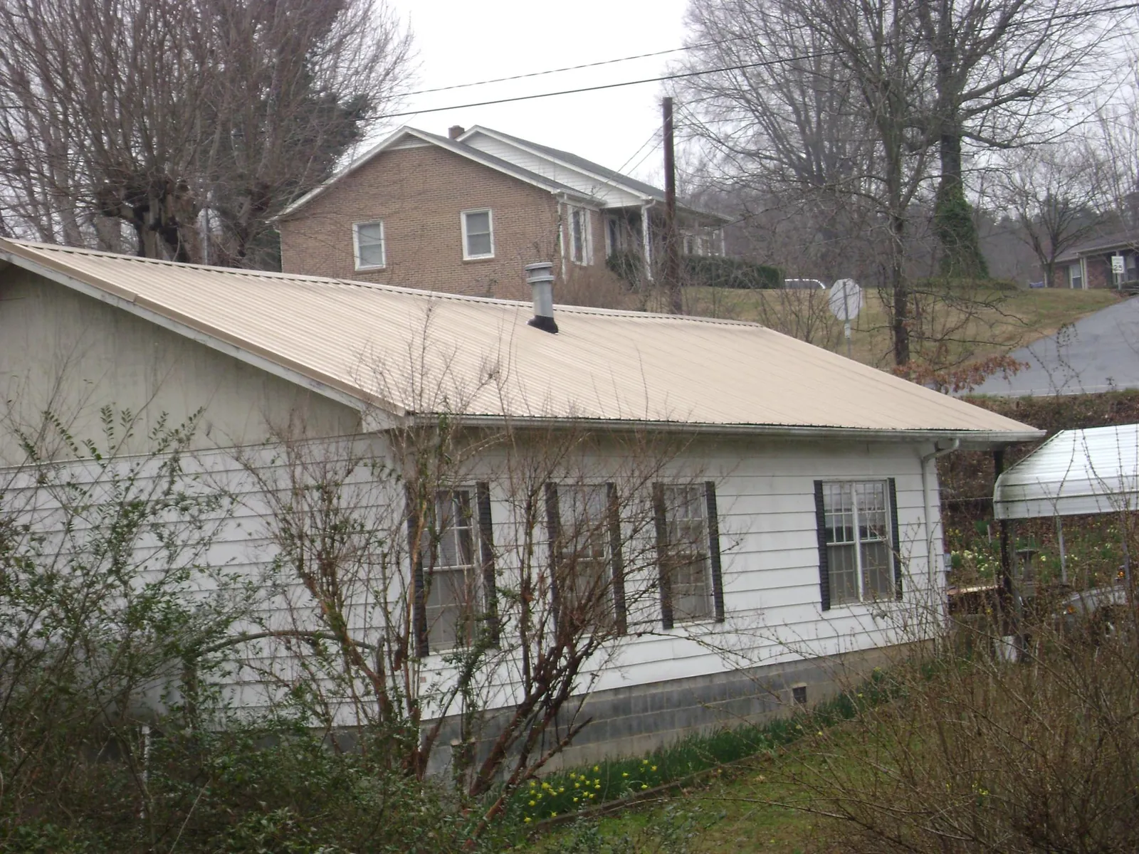Tan metal roof on a white sided house set into a hillside — Commercial Roofing by Roofing Brothers in Gladwyne